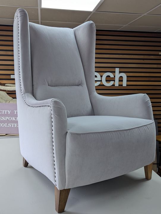 High-backed wing chair in dove-grey velvet, edged with studs